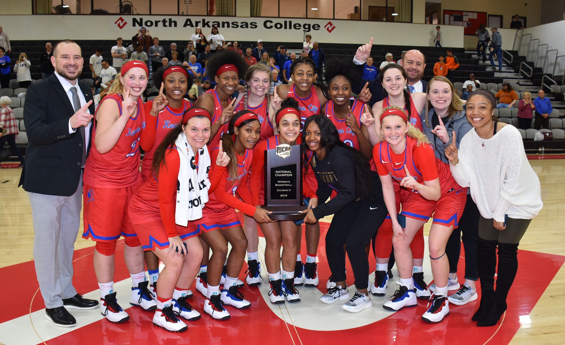 Women's basketball players standing in gym, smiling and holding trophy.