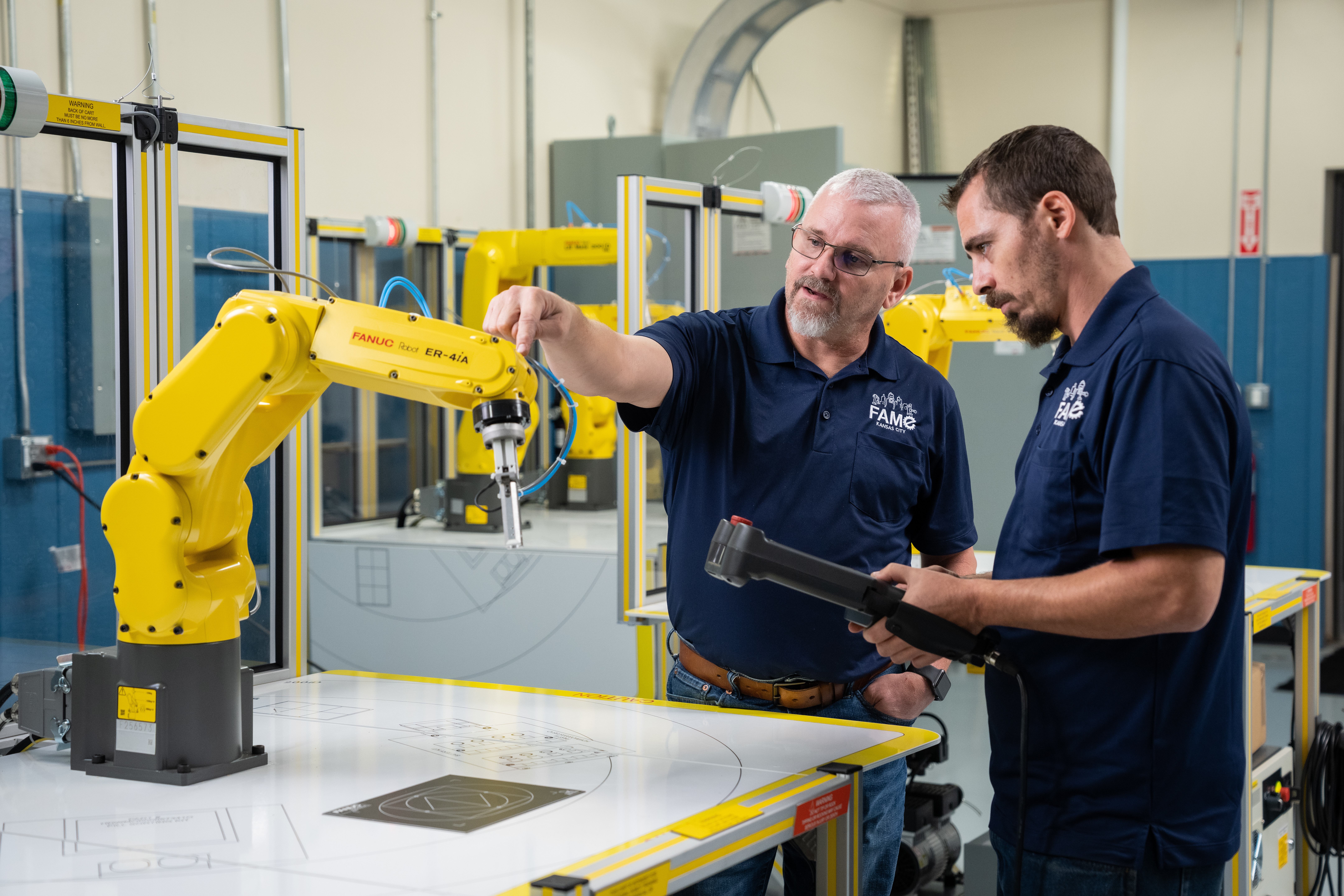 Instructor in blue shirt showing a student how to use a robotic arm.