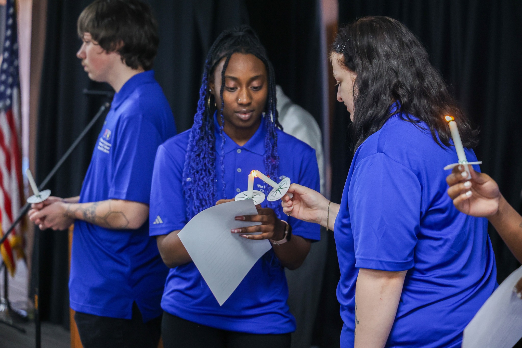 Two students in blue polo shirts lighting a candle.