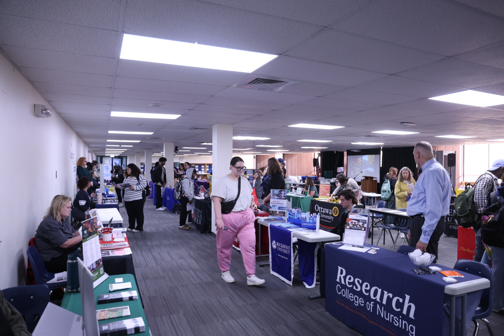 Students walking around large room speaking with college representatives.