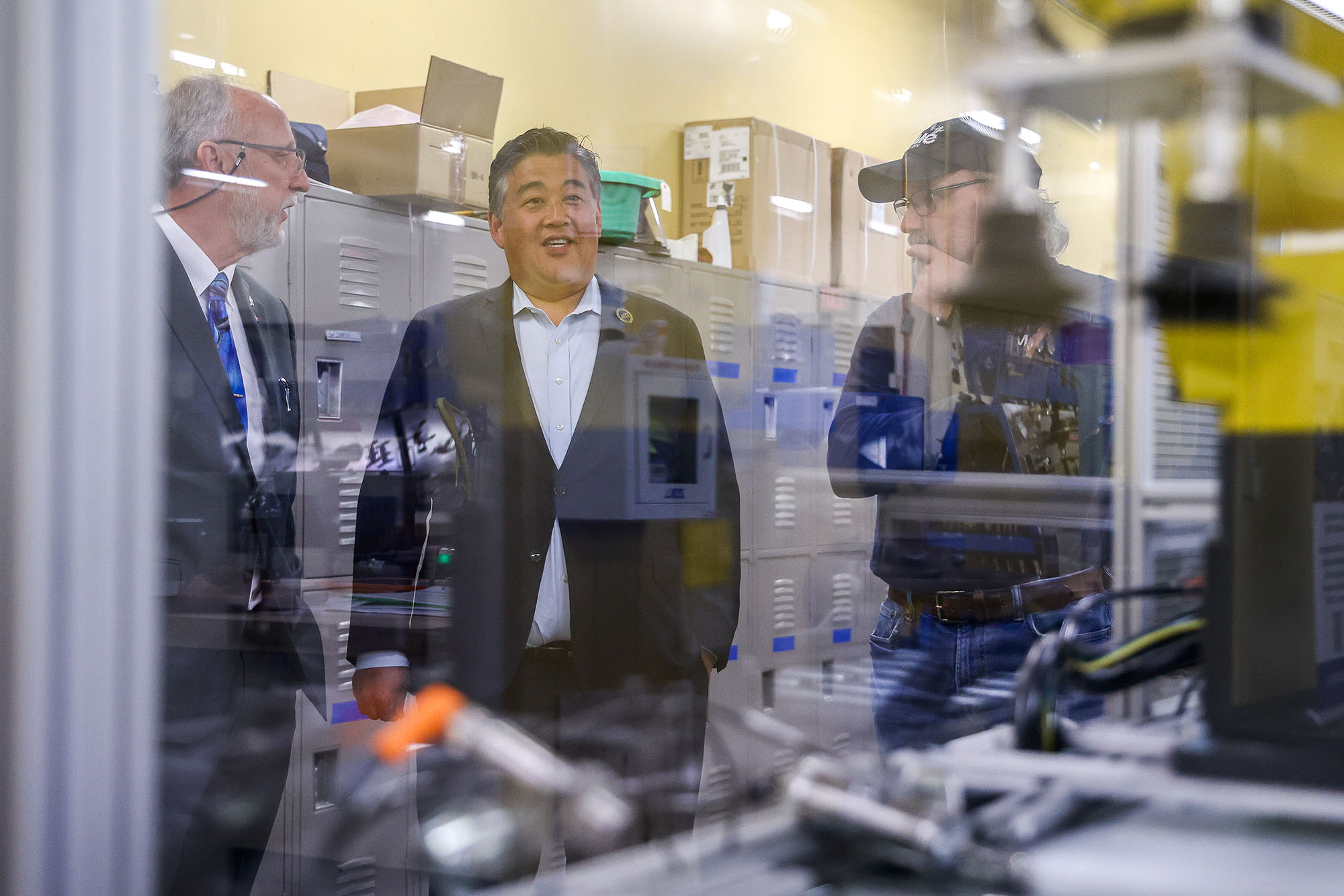 Three men stand in front of equipment talking to each other.